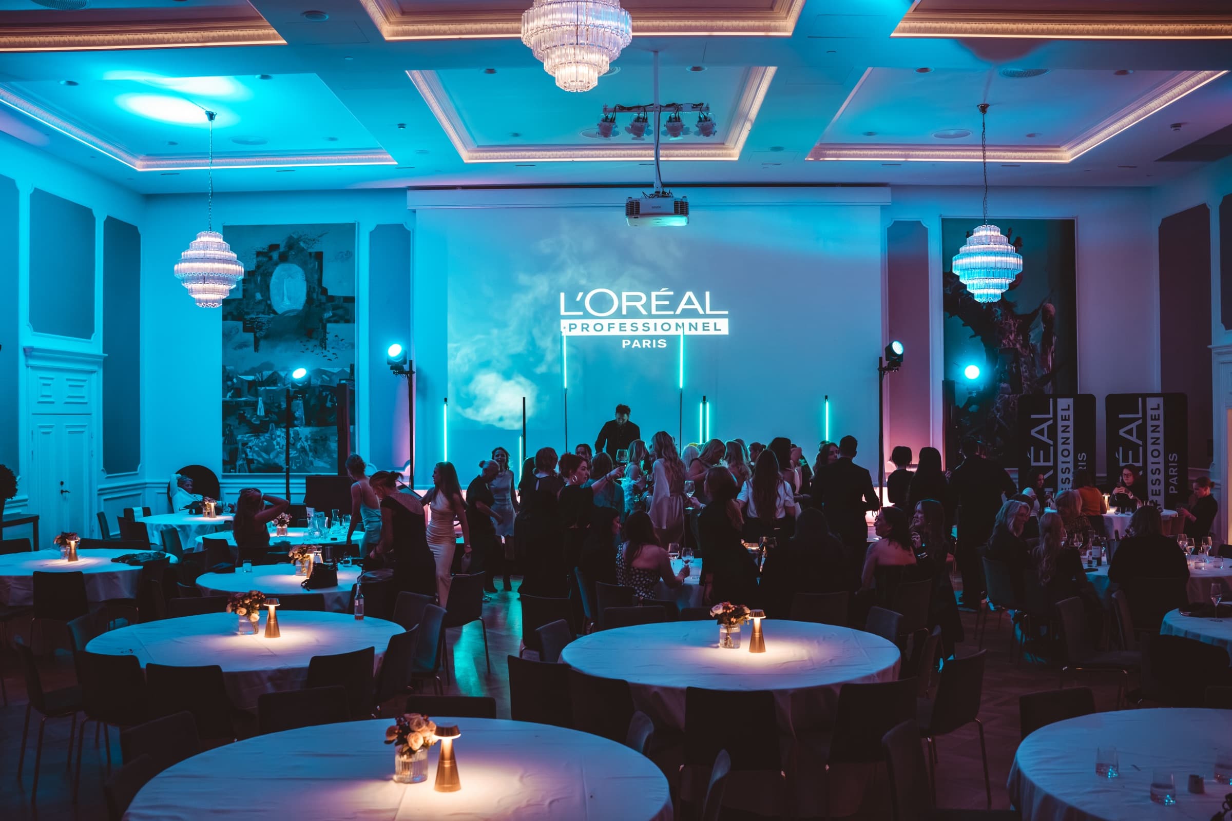 Gjester og DJ på et bedriftsarrangement for L'Oréal Professionnel Paris, med logo projisert på veggen og blått lys i salen