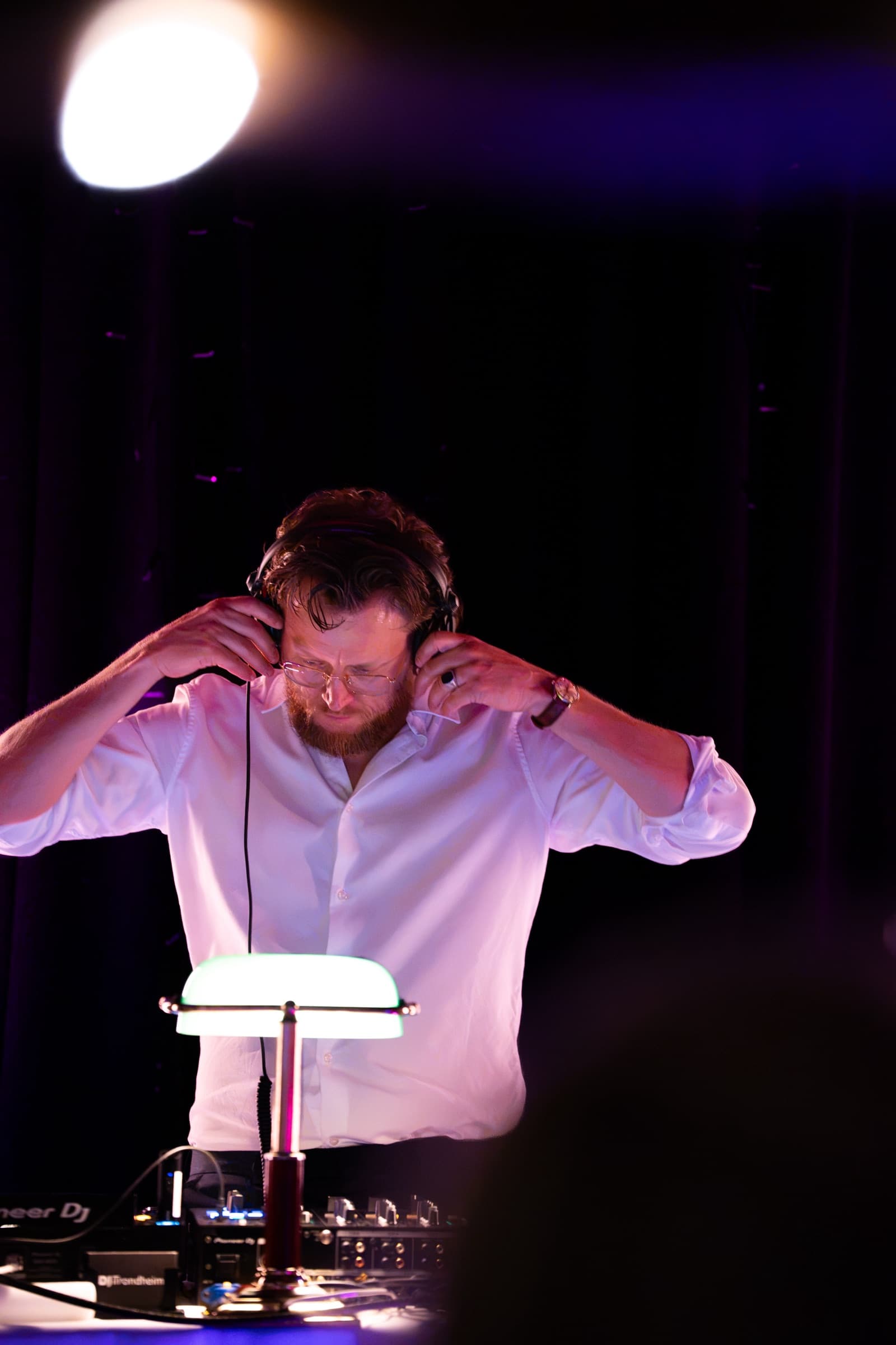 DJ justerer hodetelefonene bak pultet, med lilla scenelys under en bryllupsfest