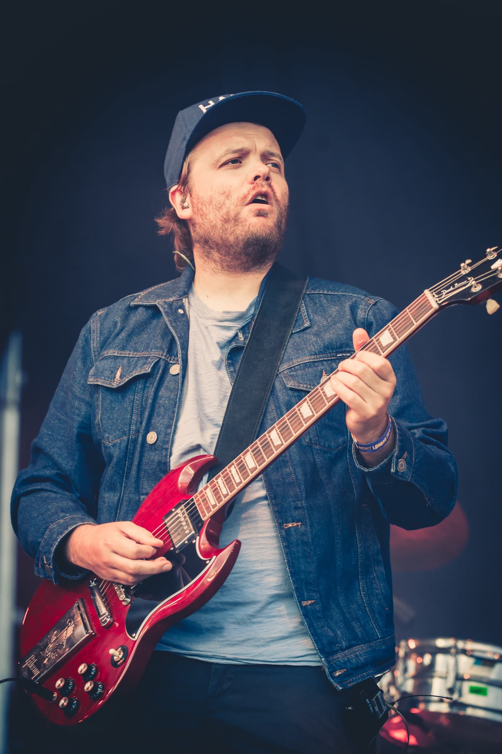 Gitarist på scenen i denimjakke, fotografert mot en mørk bakgrunn